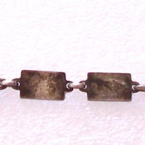 Peut inclure: Un bracelet cha&icirc;ne argent&eacute; avec des maillons rectangulaires. Le bracelet est dot&eacute; d'un petit fermoir &agrave; une extr&eacute;mit&eacute; et est pr&eacute;sent&eacute; sur un fond blanc. Les maillons semblent ternis, ce qui lui donne un aspect vintage.