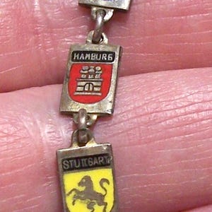 Peut inclure: Bracelet argent&eacute; compos&eacute; de breloques rectangulaires avec des armoiries &eacute;maill&eacute;es. Les breloques affichent les noms et les embl&egrave;mes des villes allemandes : Salzbourg, Bonn, Hambourg, Stuttgart et Monchen.