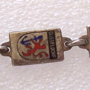 Peut inclure: Bracelet argent&eacute; compos&eacute; de breloques rectangulaires &eacute;maill&eacute;es aux couleurs vives. Chaque breloque repr&eacute;sente un embl&egrave;me de ville, dont Mayence et Cologne. Le bracelet est reli&eacute; par des maillons et poss&egrave;de un fermoir.
