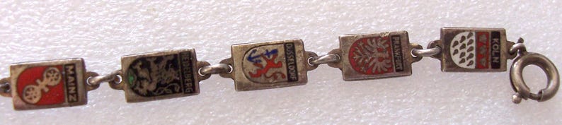 Peut inclure: Bracelet argent&eacute; compos&eacute; de breloques rectangulaires &eacute;maill&eacute;es aux couleurs vives. Chaque breloque repr&eacute;sente un embl&egrave;me de ville, dont Mayence et Cologne. Le bracelet est reli&eacute; par des maillons et poss&egrave;de un fermoir.