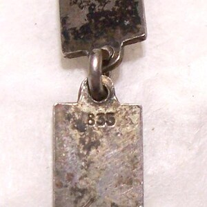 Peut inclure: Gros plan sur un collier argent&eacute; avec des maillons rectangulaires. Les maillons sont reli&eacute;s par de petits anneaux. Le fermoir est un anneau &agrave; ressort circulaire. Le chiffre "835" est visible sur l'un des maillons.