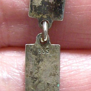 Peut inclure: Gros plan sur un collier en argent avec des maillons rectangulaires. Les maillons sont ternis, montrant des signes d'&acirc;ge. Un maillon est estampill&eacute; du num&eacute;ro "835". Le collier a un fermoir &agrave; ressort.