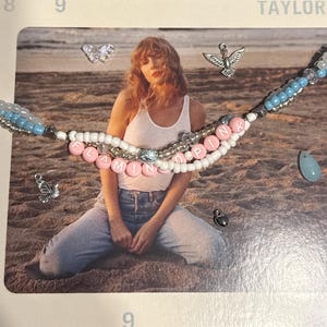 May include: A beaded necklace with the words "FLAMINGO PINK" spelled out in pink letter beads. The necklace has white and blue beads, with silver accents. Additional charms include a butterfly, a dove, and a teardrop-shaped bead.