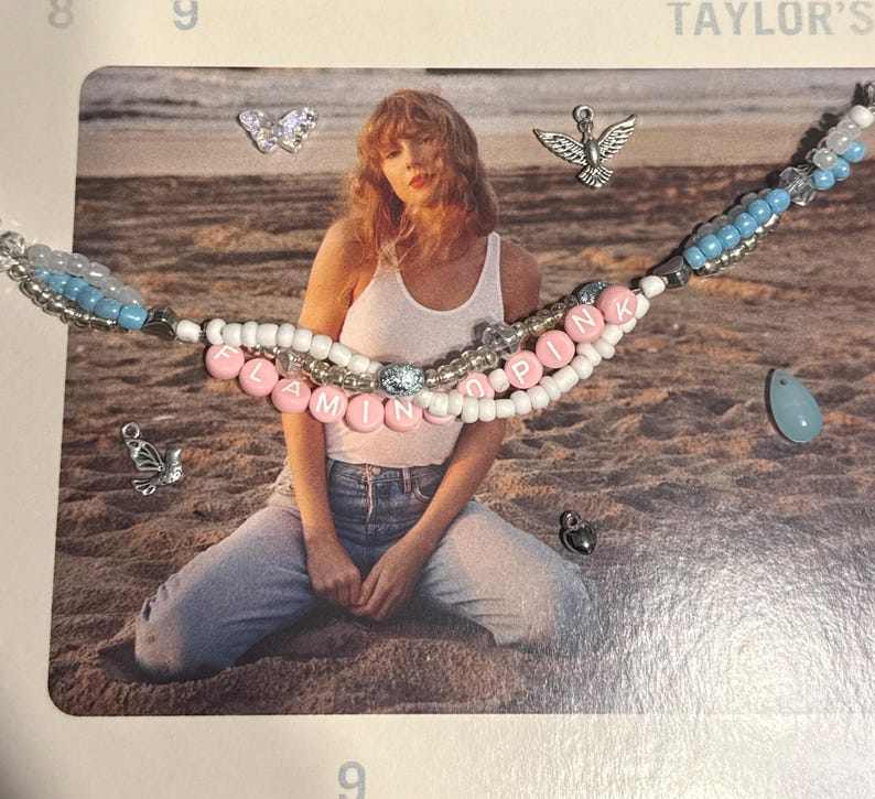 May include: A beaded necklace with the words "FLAMINGO PINK" spelled out in pink letter beads. The necklace has white and blue beads, with silver accents. Additional charms include a butterfly, a dove, and a teardrop-shaped bead.