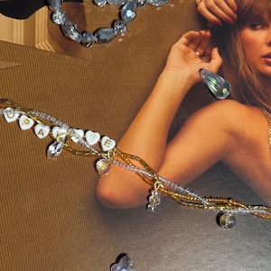 Puede incluir: Una pulsera de m&uacute;ltiples hilos con cuentas doradas, transparentes y blancas. La pulsera presenta dijes en forma de coraz&oacute;n que deletrean "cupcake" y est&aacute; adornada con detalles de cristal. Joyas de cuentas adicionales y adornos de cristal est&aacute;n dispersos.