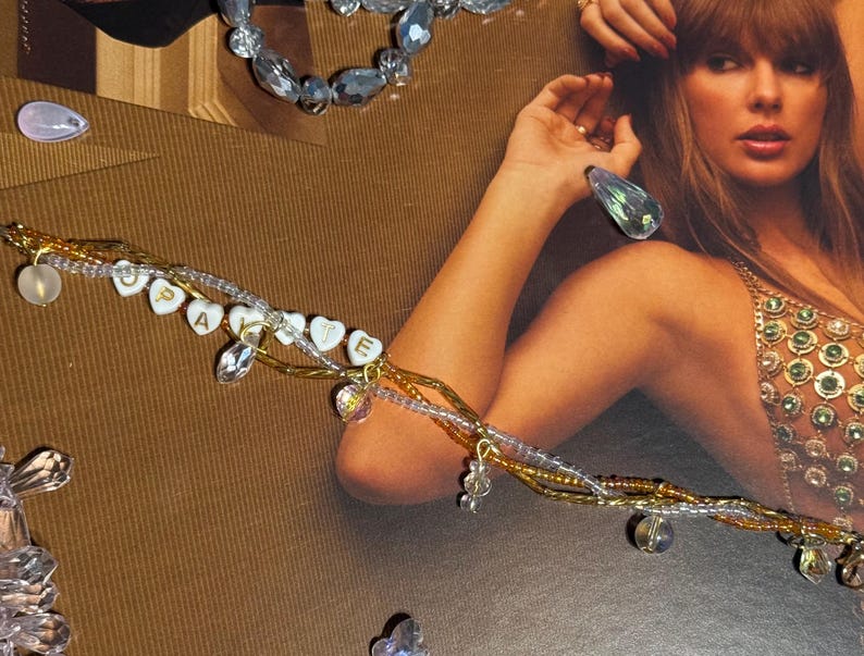 Puede incluir: Una pulsera de m&uacute;ltiples hilos con cuentas doradas, transparentes y blancas. La pulsera presenta dijes en forma de coraz&oacute;n que deletrean "cupcake" y est&aacute; adornada con detalles de cristal. Joyas de cuentas adicionales y adornos de cristal est&aacute;n dispersos.