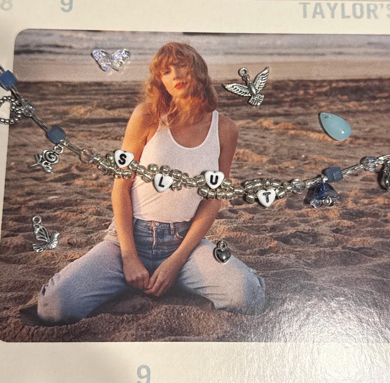 May include: A silver beaded bracelet with the letters "S L U T" spelled out in white heart-shaped beads. The bracelet also features charms of birds, butterflies, and a heart. The background shows a person sitting on a beach.