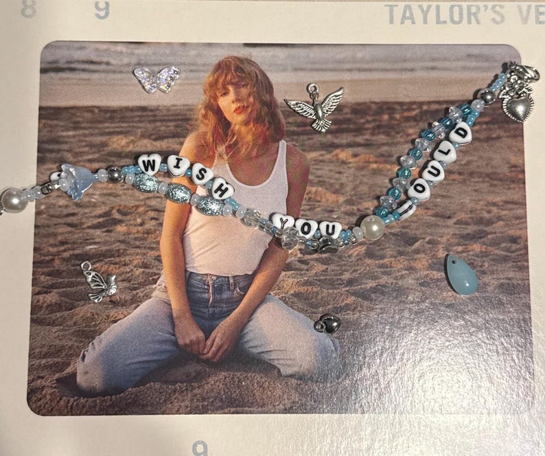 May include: A beaded bracelet with the words "WISH YOU COULD" in white letter beads, accented with blue beads and charms. The bracelet is displayed on a photograph with a beach scene and a person wearing a white tank top and jeans.