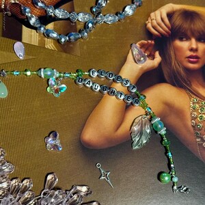 Puede incluir: Una pulsera de cuentas con las palabras "ELDEST DAUGHTER" escritas con cuentas de letras plateadas. La pulsera presenta cuentas verdes y transparentes, dijes de mariposa y un dije de hoja. Tambi&eacute;n se ven joyas de cuentas adicionales.