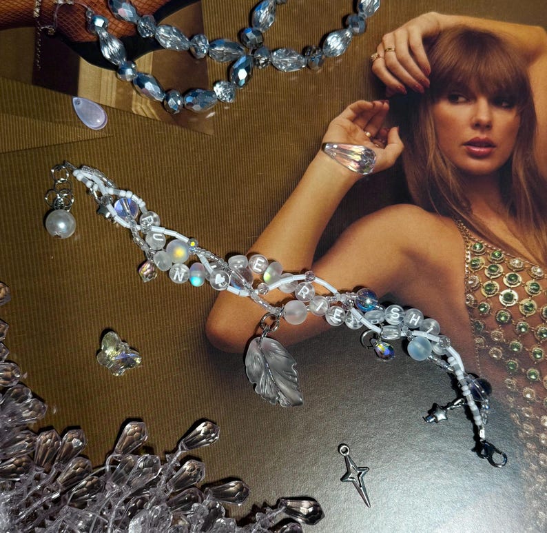 Puede incluir: Una colecci&oacute;n de joyas de cuentas transparentes e iridiscentes. Las piezas incluyen una pulsera que deletrea "CHERISH", un collar y un anillo. La pulsera presenta un dije de hoja y un dije de estrella. Las joyas est&aacute;n sobre un fondo dorado.