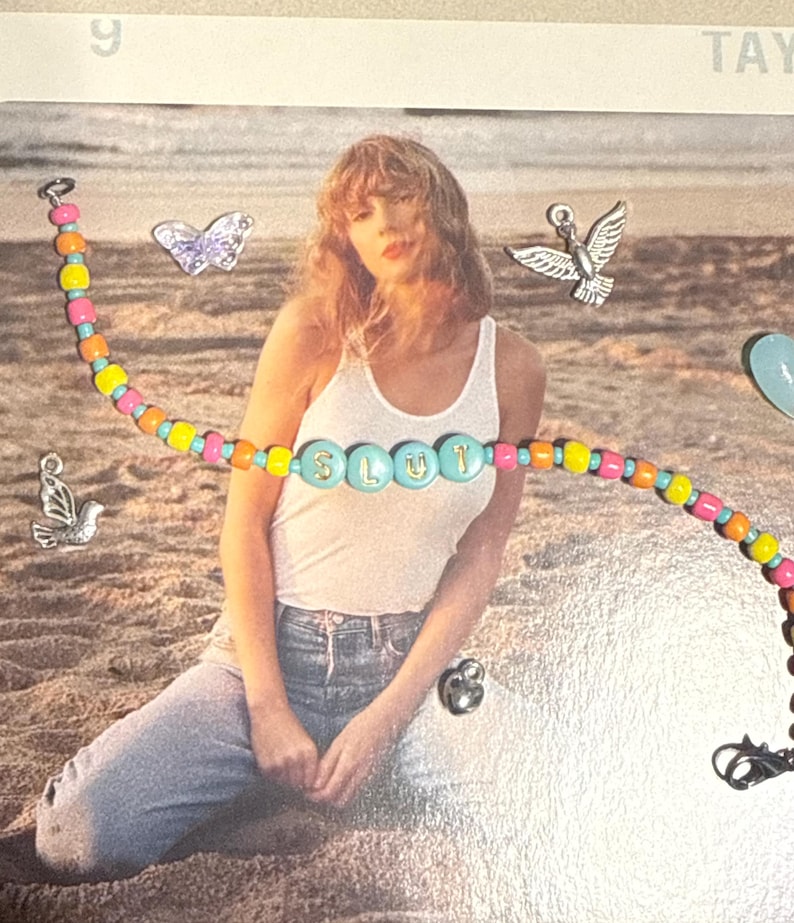 May include: A colorful beaded bracelet with the word "SLUT" spelled out in turquoise beads. The bracelet features a mix of orange, pink, yellow, and turquoise beads. The background includes a person wearing a white tank top and blue jeans.