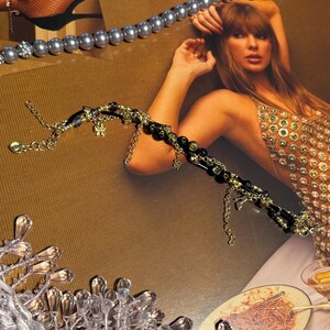 Puede incluir: Una pulsera de cuentas doradas y negras con dijes colgantes, incluyendo una serpiente y una flor. Tambi&eacute;n se ven un collar de perlas y un collar plateado con detalles de cristal. La imagen tiene un fondo marr&oacute;n.