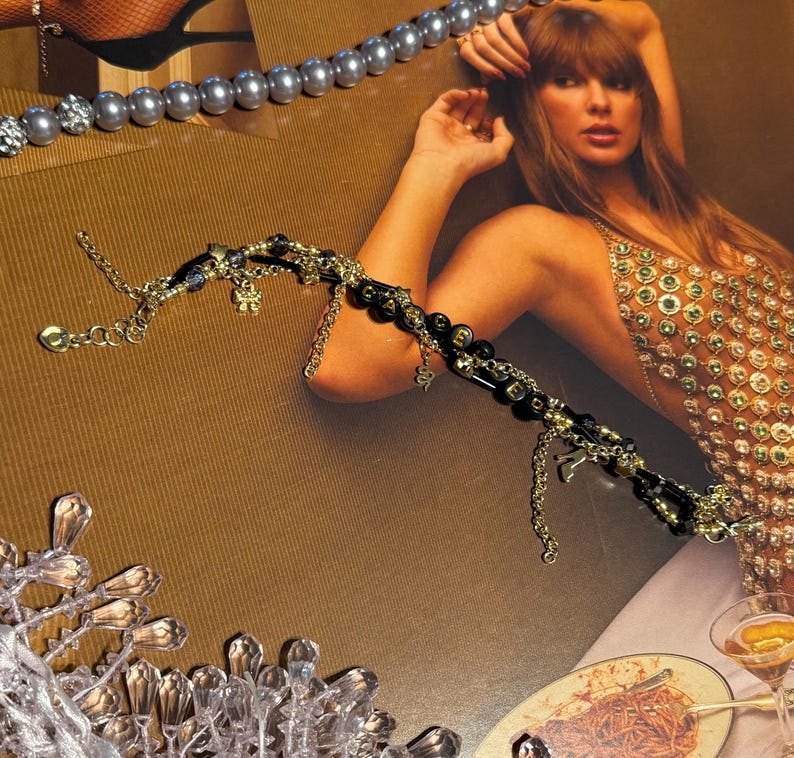 Puede incluir: Una pulsera de cuentas doradas y negras con dijes colgantes, incluyendo una serpiente y una flor. Tambi&eacute;n se ven un collar de perlas y un collar plateado con detalles de cristal. La imagen tiene un fondo marr&oacute;n.