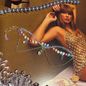 Puede incluir: Un collar dorado con las palabras "SEQUINS ARE FOREVER" en cuentas de letras coloridas. El collar tiene colgantes. Una collar de perlas est&aacute; en la parte superior de la imagen. El fondo es de color marr&oacute;n.