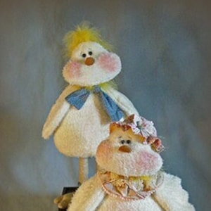 Puede incluir: Dos pollos de peluche blancos con mejillas rosadas y picos amarillos. El pollo de la izquierda tiene una corbata de lazo azul y el pollo de la derecha tiene una corbata de lazo rosa y amarilla. Ambos pollos tienen patas largas y están de pie sobre una caja de madera.