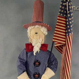 May include: A handmade doll dressed as Uncle Sam, wearing a red, white, and blue top hat, a blue jacket with white polka dots, red and white striped pants, and white gloves. The doll is holding a wooden staff with an American flag attached to it. The flag is red, white, and blue with white stars on a blue field. The doll is standing on a wooden base. The text "Uncle Sam" is written in white on a blue background above the doll.