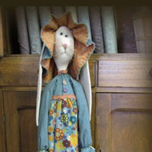 May include: A handmade bunny doll wearing a blue and floral dress with a white lace collar. The doll is holding a string of colorful Easter eggs.