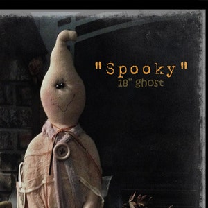 May include: A handmade 18-inch ghost doll with a white fabric body and a button nose. The doll is wearing a white fabric dress and has a black fabric "Spooky" sign hanging from its neck. The doll is sitting on a wooden surface with a brown background.