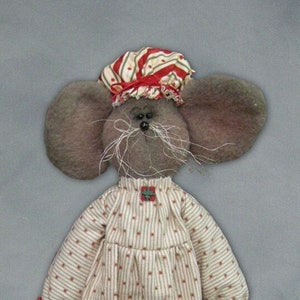 May include: A gray mouse doll wearing a red and white striped nightcap and a white and red polka dot nightgown. The doll is holding a red and white striped pillow and is wearing pink slippers.