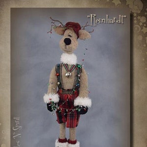 May include: A handmade plush reindeer doll wearing a red and black plaid outfit, a red hat, and a string of Christmas lights. The doll is standing on a gray background and has the text "Reinhardt" above it. The doll is a pattern from Sparkles N' Sprinkles, a doll pattern company.