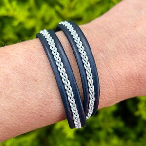May include: A double wrap bracelet with a navy blue leather band and a silver braided design.