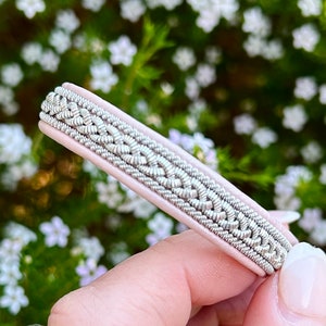 May include: A pink leather bracelet with a silver braided design.