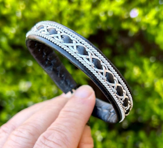 Nordic Sami leather bracelet with traditional braiding using flat pewter threads and borders. Unisex wristband accessory.