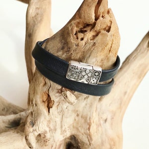 May include: A black leather double wrap bracelet with a silver magnetic clasp featuring a geometric design.