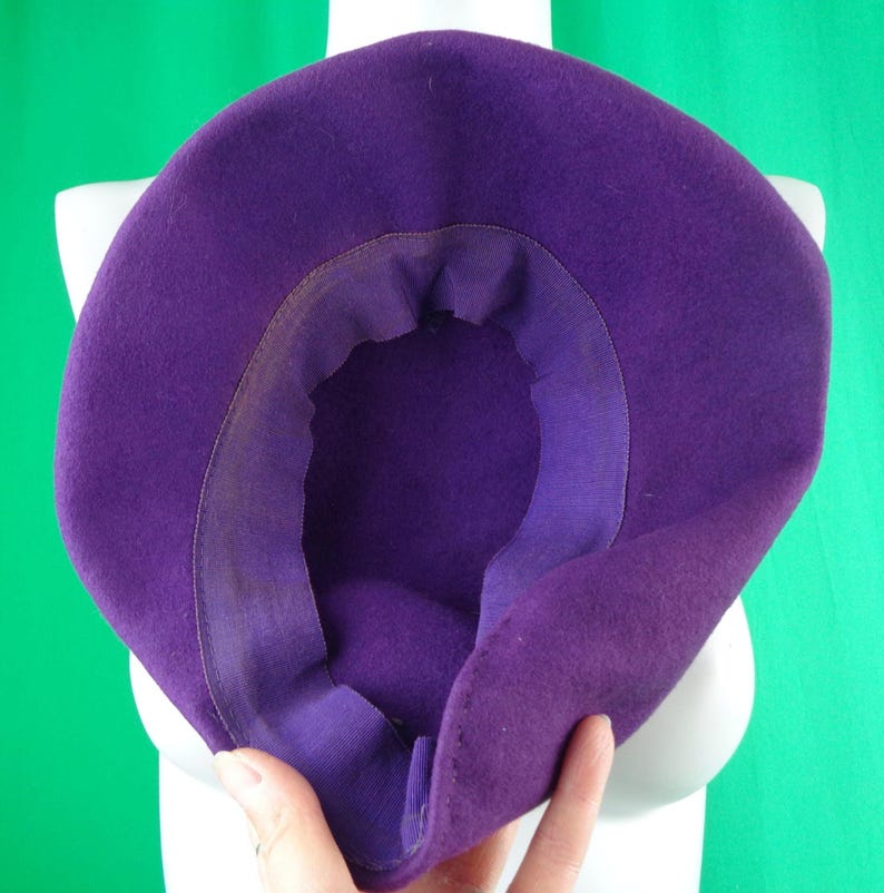 Peut inclure: Un chapeau en feutre violet profond vu de l'int&eacute;rieur, r&eacute;v&eacute;lant la calotte et la doublure int&eacute;rieure du bord. Le chapeau pr&eacute;sente un mat&eacute;riau en feutre lisse de couleur unie avec une bande en tissu violet assortie cousue le long de la circonf&eacute;rence.