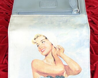 May include: A light blue wallet featuring a printed illustration of a smiling person with blonde hair wearing a white head covering and a white top with blue floral accents. The interior includes a zippered compartment and a Relic brand label.