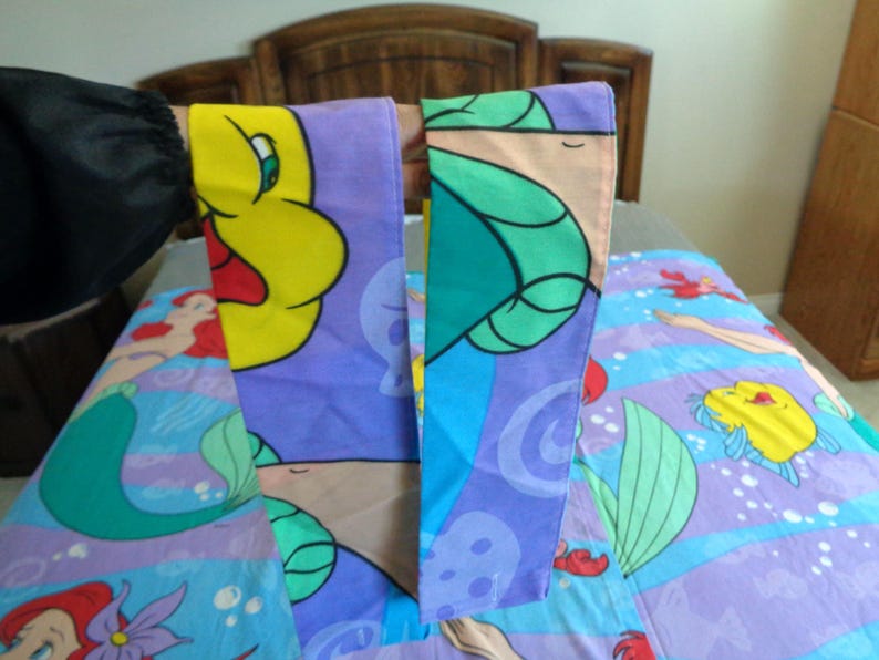 May include: A bed set featuring characters from The Little Mermaid. The set includes a pillowcase with a yellow character and a blue and purple comforter with Ariel and Flounder. The bedding has a cartoon style.