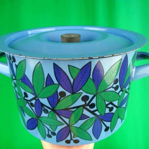 May include: A light blue enamel pot with a matching lid and handles. The pot is decorated with a pattern of green and purple leaves and black berries. The lid has a wooden knob.