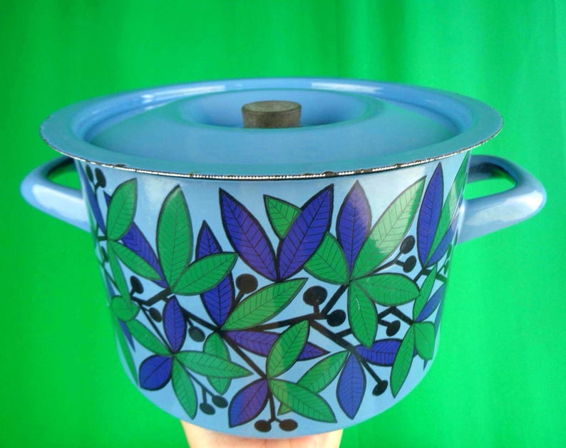 May include: A light blue enamel pot with a matching lid and handles. The pot is decorated with a pattern of green and purple leaves and black berries. The lid has a wooden knob.