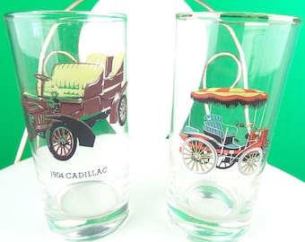 May include: Two vintage glass tumblers with illustrations of antique cars. The left tumbler features a brown 1904 Cadillac with the text "1904 CADILLAC". The right tumbler features a red car with a striped canopy.