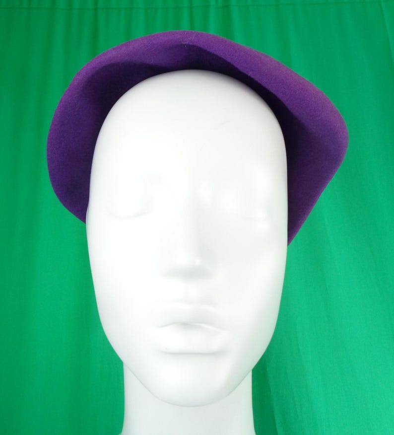 Peut inclure: Un b&eacute;ret en feutre violet uni avec une calotte arrondie et lisse et un bord l&eacute;g&egrave;rement incurv&eacute;. Le chapeau est pr&eacute;sent&eacute; sur une t&ecirc;te de mannequin blanche unie, mettant en valeur la couleur violette profonde et vibrante ainsi que la texture douce.
