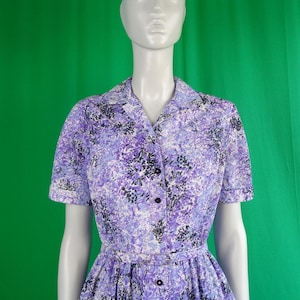 May include: A purple and white floral print dress with short sleeves and a button-up front. The dress has a fitted bodice and a full skirt.