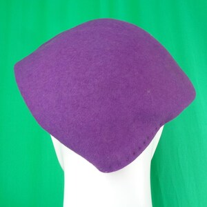 Peut inclure: Un chapeau en feutre violet uni avec une forme structur&eacute;e, angulaire et &agrave; quatre coins. Le chapeau pr&eacute;sente une texture lisse et mate ainsi qu'une s&eacute;rie de petites coutures r&eacute;guli&egrave;rement espac&eacute;es le long du bord inf&eacute;rieur.