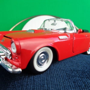 Puede incluir: Un modelo de coche de juguete rojo Ford Thunderbird convertible de la década de 1950. El coche tiene neumáticos de banda blanca y detalles cromados.