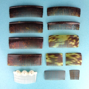 May include: A collection of vintage hair combs in various sizes and styles. The combs feature tortoiseshell patterns in shades of brown, green, and yellow. One white comb is adorned with floral embellishments. The combs are arranged on a light blue surface.