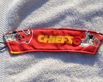 May include: Red and yellow fabric coffee cup cozy with the word "CHIEFS" and a red button. The fabric has a pattern of football helmets.
