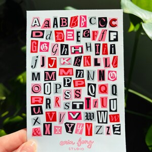 May include: A print featuring a collage of alphabet letters in various fonts and sizes, cut from different backgrounds. The letters are in shades of pink, red, black, and gray. The artist's name, "erin fong STUDIO," is printed at the bottom.