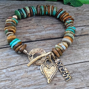 May include: A turquoise and brown stone bracelet with a gold heart charm and a gold tag that says "Dream".