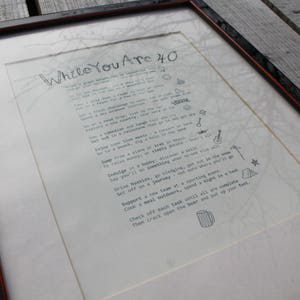 May include: A framed print with a handwritten list of things to do while you are 40. The list includes activities like "Indulge in a hobby", "Say you'll do something", "Deliver a  hike", "Set off on a journey", "Support a new team", "Cook a meal outdoors", "Check off each task until all are complete", "Then crack open the beer and put up your feet".