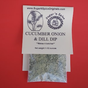 May include: A white package with a label that reads "Sugar 'n Spice" and "Cucumber Onion & Dill Dip" with the text "Makes 4 batches" and "Net weight 1-1/2 ounces". A small clear plastic bag containing a green powder mix is visible below the label.
