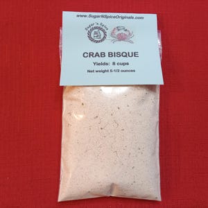 May include: A clear plastic bag containing a beige powder mix labeled "Crab Bisque" with the text "Yields: 8 cups" and "Net weight 5-1/2 ounces".