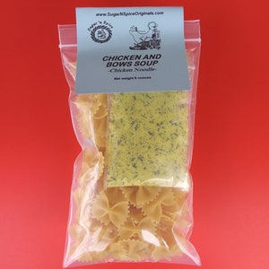 May include: A clear plastic bag containing a package of dried soup mix and a bag of uncooked bowtie pasta. The soup mix is green and yellow and the pasta is yellow. The bag has a label that reads "Chicken and Bows Soup - Chicken Noodle - Net weight 8 ounces".