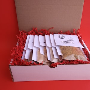 May include: A white box filled with red shredded paper and eight small white bags containing different spice blends. The bags are labeled with the names of the spices. The box is labeled "Rotisserie Chicken Rub".