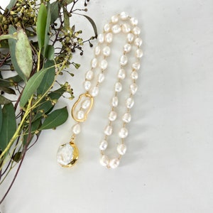 May include: A long white pearl necklace with a gold clasp and a large white pearl pendant.