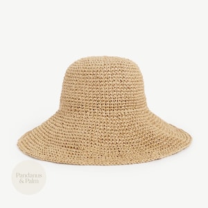 Peut inclure: Un chapeau de soleil beige tissé avec un large bord et une couronne arrondie. Le chapeau est fait d'une matière fibreuse naturelle et a un aspect texturé. Le chapeau est conçu pour protéger du soleil.