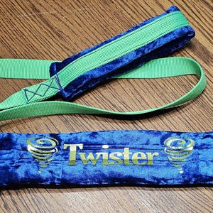 May include: A blue velvet dog toy with the word "Twister" in gold lettering. The toy has a green strap and accents. The toy is designed for dogs to play with and is made of durable materials.